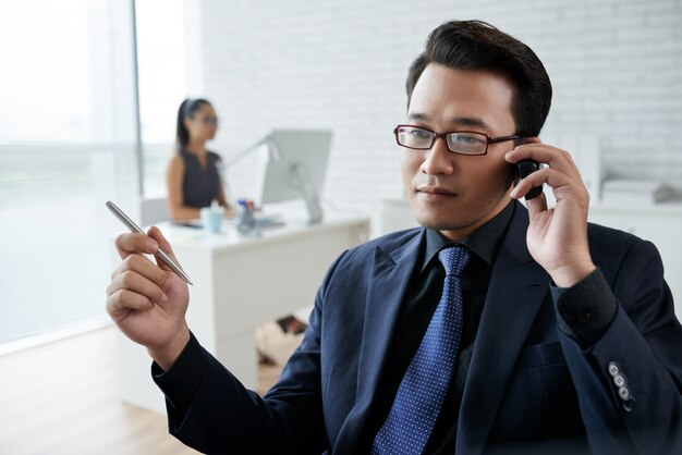 Close-up van de Aziatische mens die op de telefoon in het bureau spreekt