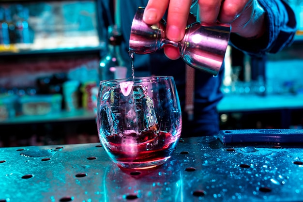 Close-up van de barman voltooit de voorbereiding van een alcoholische cocktail, het gieten van een drankje in neonlicht