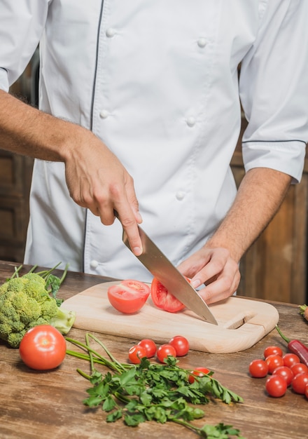 Close-up van de hand die van de chef-kok rode tomaat op hakbord snijdt