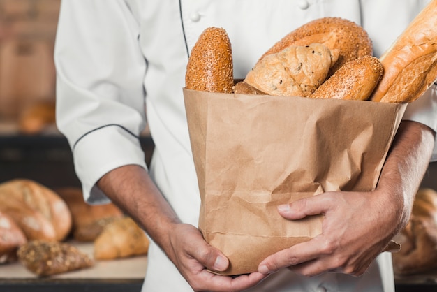 Close-up van de hand die van de mannelijke bakker gebakken brood in een document zak houdt