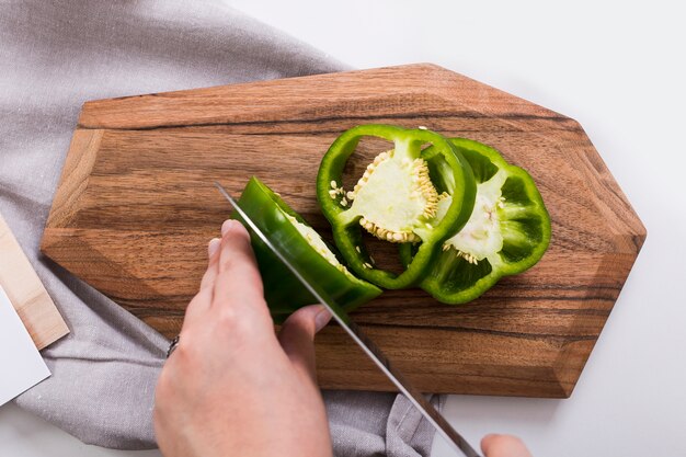 Close-up van de hand die van de vrouw de groene paprika met scherp mes op hakbord snijdt