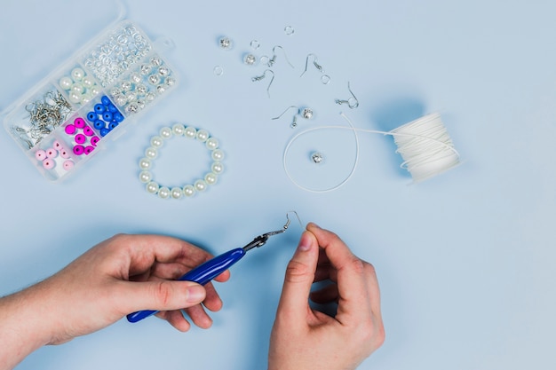 Close-up van de hand die van de vrouw de oorringen en de armband met parels op blauwe achtergrond maakt