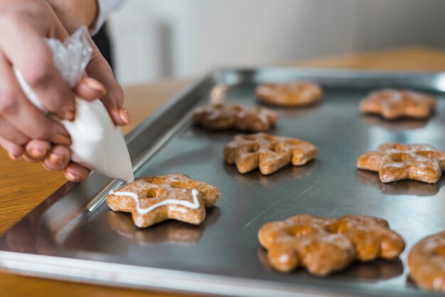 Close-up van de hand die van de vrouw room op traditioneel Kerstmiskoekje over het bakseldienblad drukt