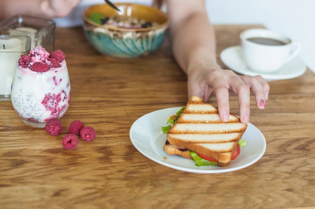 Close-up van de hand die van de vrouw sandwich van ceramische plaat op houten lijst neemt