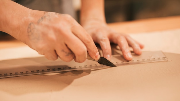 Close-up van de hand die van de vrouwelijke pottenbakker de klei met heerser en hulpmiddel snijdt