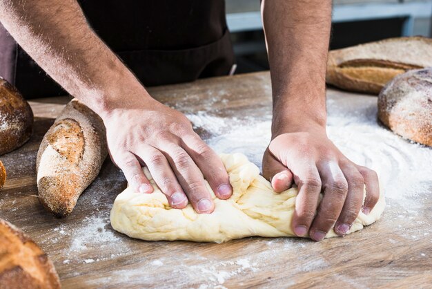 Close-up van de hand die van een mannelijke bakker het deeg op lijst kneden