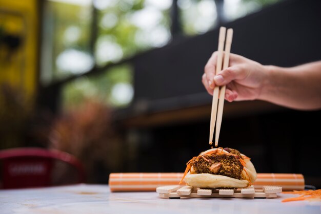 Close-up van de hand die van een persoon gua bao met eetstokjes op houten dienblad eet