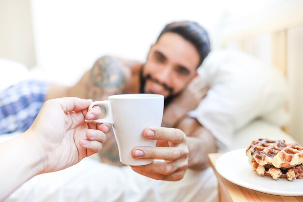 Close-up van de hand die van een persoon kop van koffie geeft aan de jonge mens