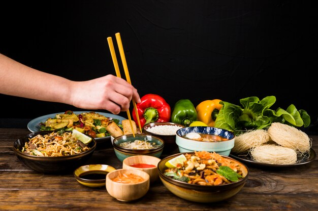 Close-up van de hand die van een persoon Thais voedsel met eetstokjes op lijst eet tegen zwarte achtergrond