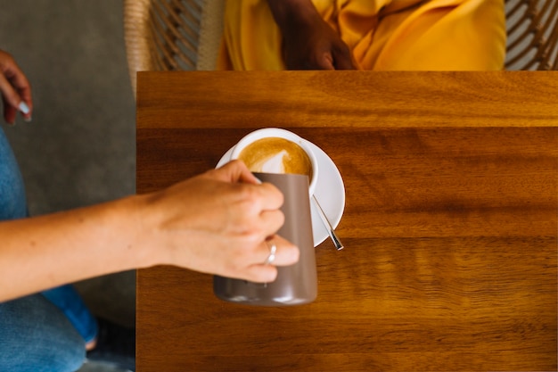 Close-up van de hand gietende melk van de vrouw in de kop op lijst