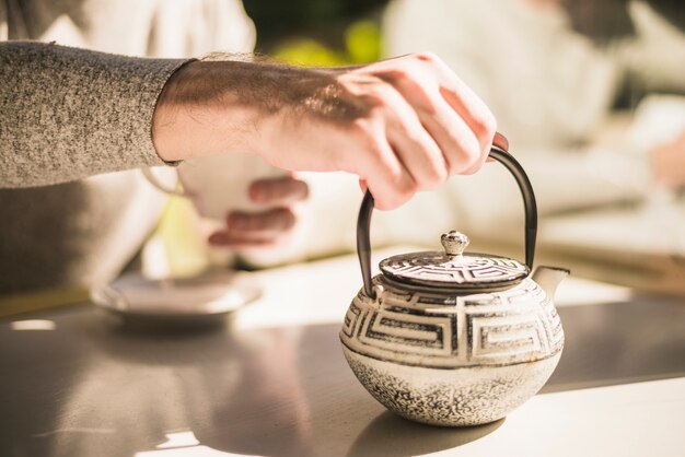 Close-up van de hand met traditionele waterkoker op tafel