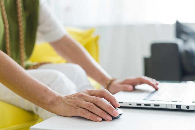 Close-up van de hand van de hogere vrouw gebruikend muis en laptop