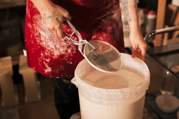 Close-up van de hand van de vrouwelijke pottenbakker die het servies in verfemmer opneemt