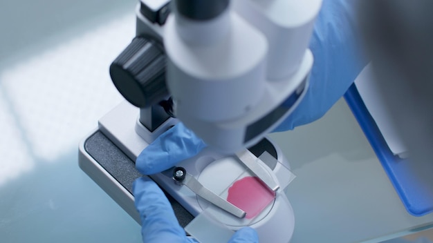 Close-up van de hand van de wetenschapper arts die de medische microscoop aanpast die dia met bloedmonster analyseert die werkt aan de ontwikkeling van vaccins tijdens het scheikunde-experiment in het ziekenhuislaboratorium. geneeskunde concept