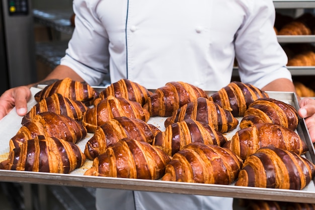 Close-up van de hand van een mannelijke bakker die vers gebakken croissantendienblad houdt