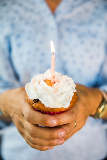 Close-up van de hand van een persoon die een cupcake met verlichte kaars