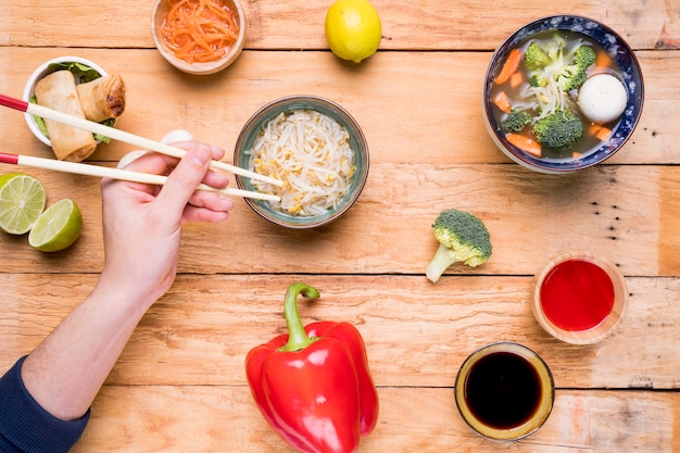 Close-up van de hand van een persoon die Thaise bonenspruiten met eetstokjes op lijst eet