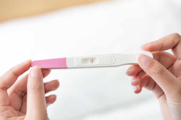 Close-up van de hand van een vrouw die een zwangerschapstestkit omhoog houdt met een negatief resultaat