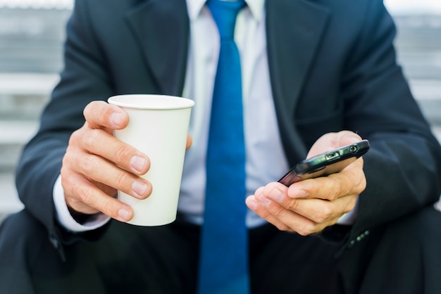 Close-up van de hand van een zakenman met een kopje koffie en mobiele telefoon