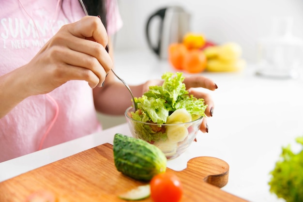 Close-up van de handen die van de vrouw salade in de keuken mengen