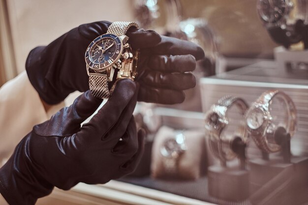 Close-up van de handen van de verkoper in handschoenen toont het exclusieve herenhorloge uit de nieuwe collectie in de luxe juwelierszaak