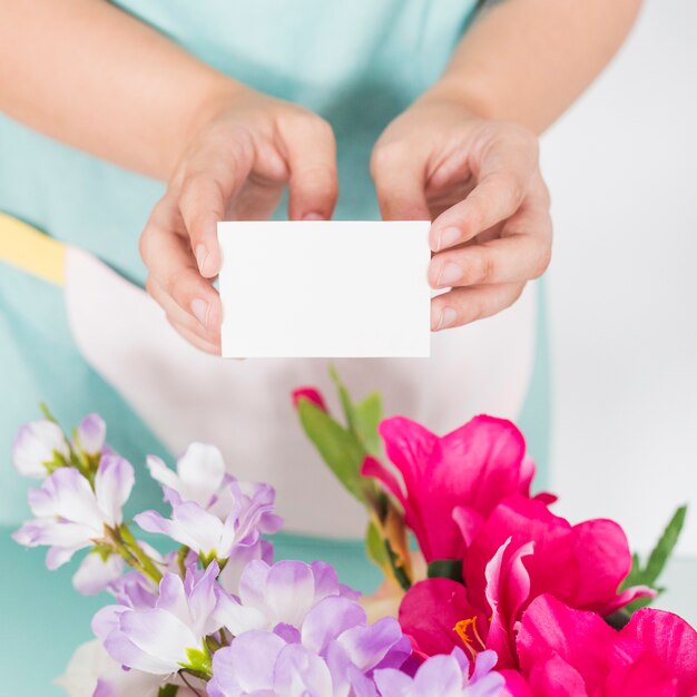 Close-up van de handholding van een vrouw leeg visitekaartje over kleurrijke bloemen