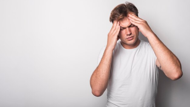 Close-up van de jonge mens die aan hoofdpijn lijdt die over witte achtergrond wordt geïsoleerd