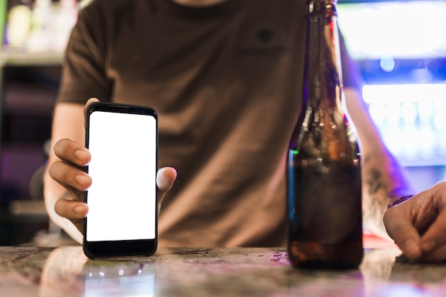 Gratis foto close-up van de mens die lege witte mobiele scherm met bierfles op tafel