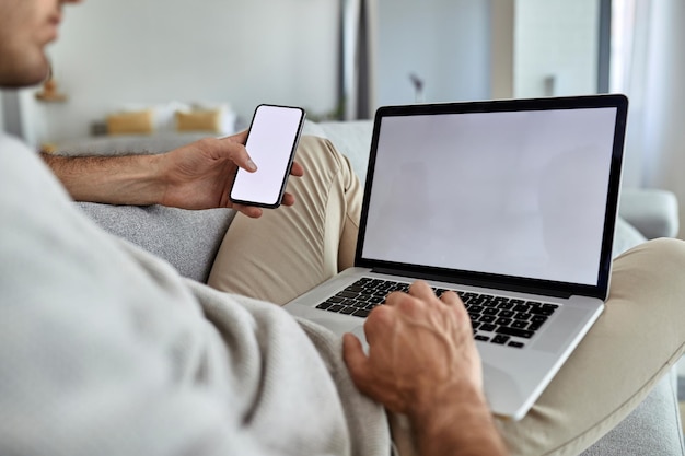 Close-up van de mens die op de bank ontspant en mobiele telefoon en laptop gebruikt Ruimte kopiëren