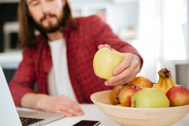 Close-up van de mens die vruchten eten en laptop thuis met behulp van