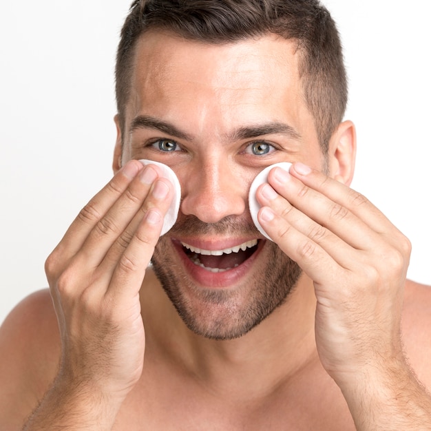 Close-up van de mens die zijn gezicht met katoenen stootkussen en het glimlachen schoonmaakt