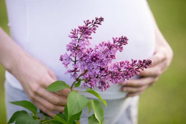 Close-up van de torso van een zwangere vrouw die lila bloem buiten heeft