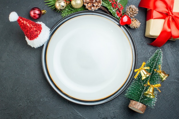 Close-up van diner plaat kerstboom fir takken conifer kegel geschenkdoos kerstman hoed op zwarte achtergrond
