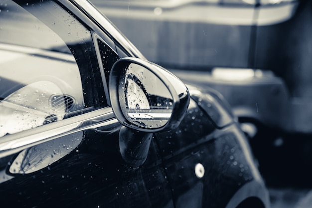 Close-up van een achteruitkijkspiegel van een zwarte auto bedekt met regendruppels