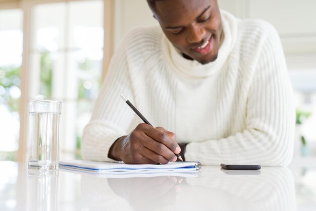 Close-up van een afrikaanse man die een briefje schrijft op een papier met een zelfverzekerde glimlach