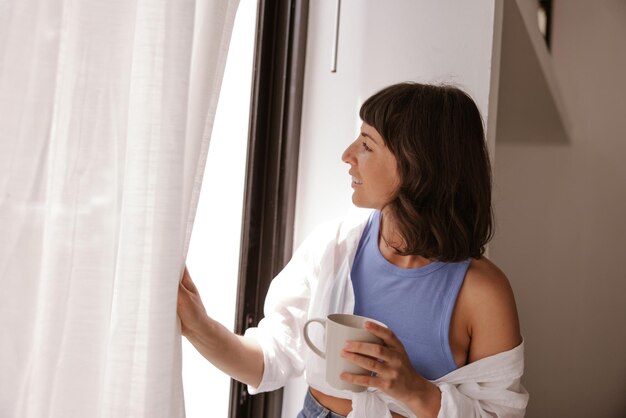 Close-up van een blanke vrouw die naar een beker kijkt met een raam