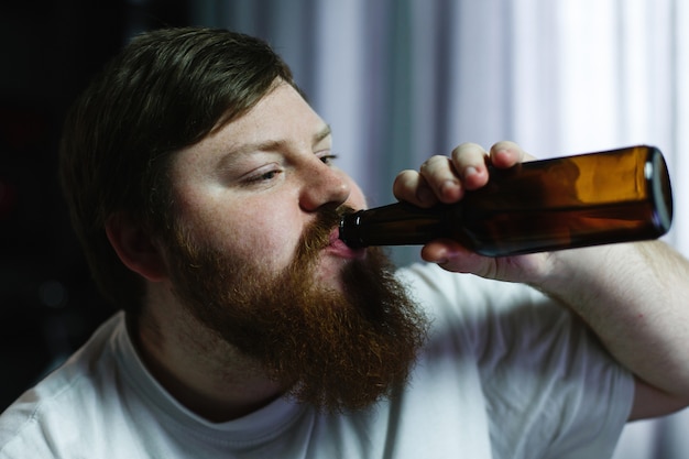 Close-up van een dikke man op zoek lelijk, terwijl hij bier drinkt