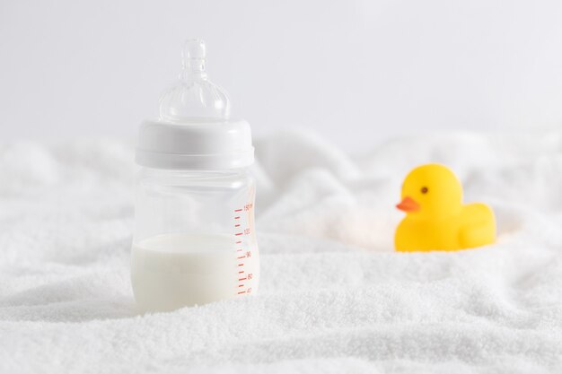 Close-up van een fles melk naast een speelgoed eend op een wit oppervlak