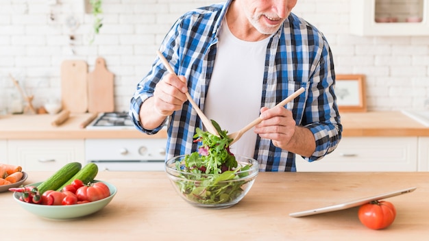 Close-up van een gelukkige hogere mens die de salade in de keuken voorbereidt