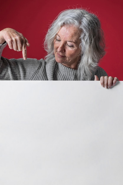 Close-up van een hogere vrouw die op zwart wit aanplakbord over rode oppervlakte richt