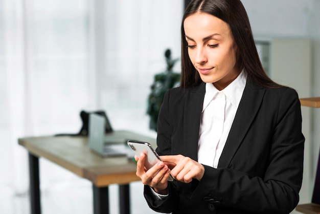 Close-up van een jonge onderneemster die zich in het bureau wat betreft smartphone bevindt