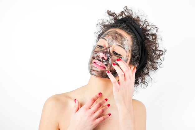 Close-up van een jonge vrouw die zwart masker toepast tegen witte achtergrond