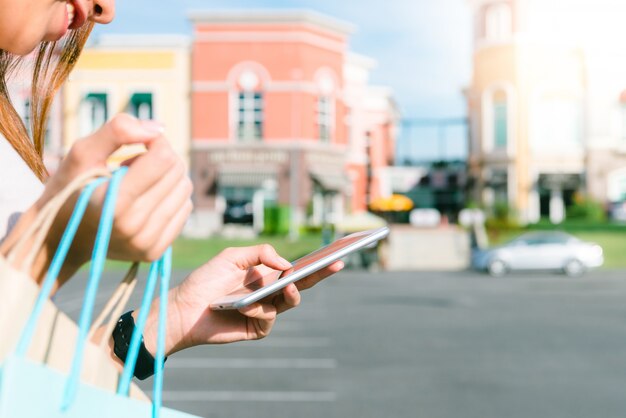 Close-up van een jonge vrouw houdt een boodschappentassen in haar hand en chatten op haar telefoon na het winkelen