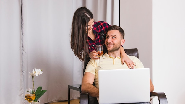 Close-up van een jonge vrouw met wijnglas in de hand staande achter de man met behulp van laptop