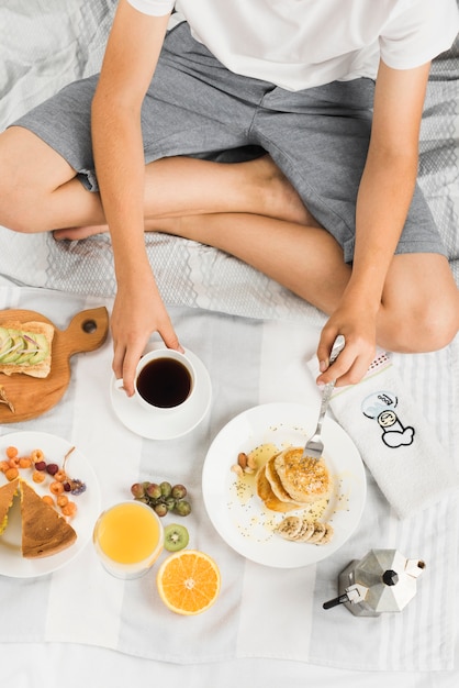 Close-up van een jongen zittend op bed met pannenkoek en koffie