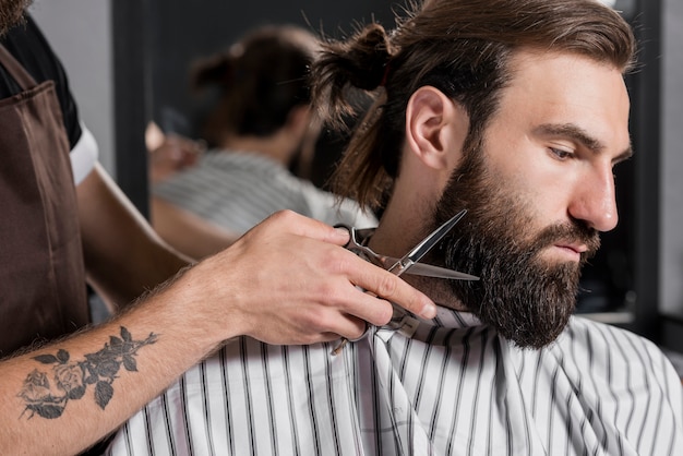 Close-up van een kapper die de baard van de mannelijke klant snijdt