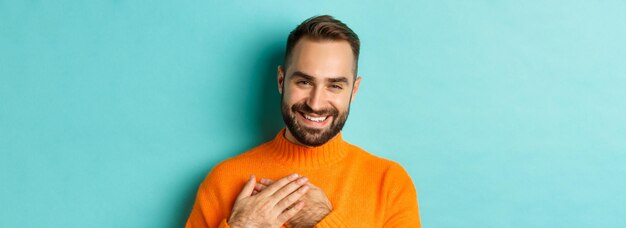 Close-up van een knappe jonge man die dank u zegt, hand in hand op het hart en glimlachend dankbaar staand