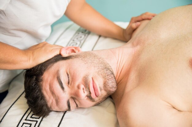 Close-up van een knappe Latijnse man die een massage op zijn nek krijgt terwijl hij ontspant in een kuuroord