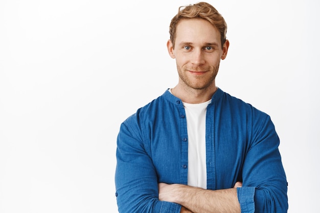 Close-up van een knappe professionele man die zijn armen op zijn borst kruist en zelfverzekerd naar de camera kijkt, vastberaden glimlachend en tegen een witte achtergrond staat