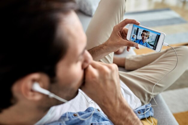 Close-up van een man die hoest terwijl hij een smartphone gebruikt en online met zijn arts praat vanuit huis